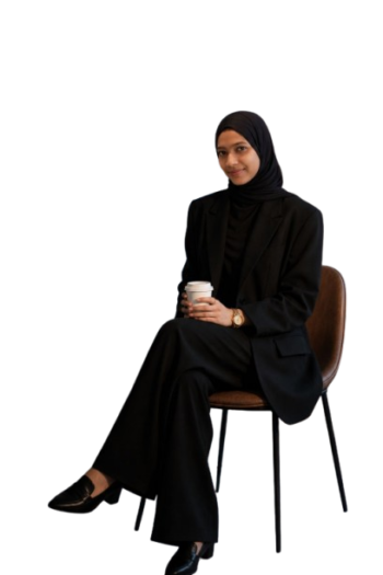Shaziya N.E., a digital marketing strategist, sitting on a chair and holding a coffee cup against a green background on her professional website.